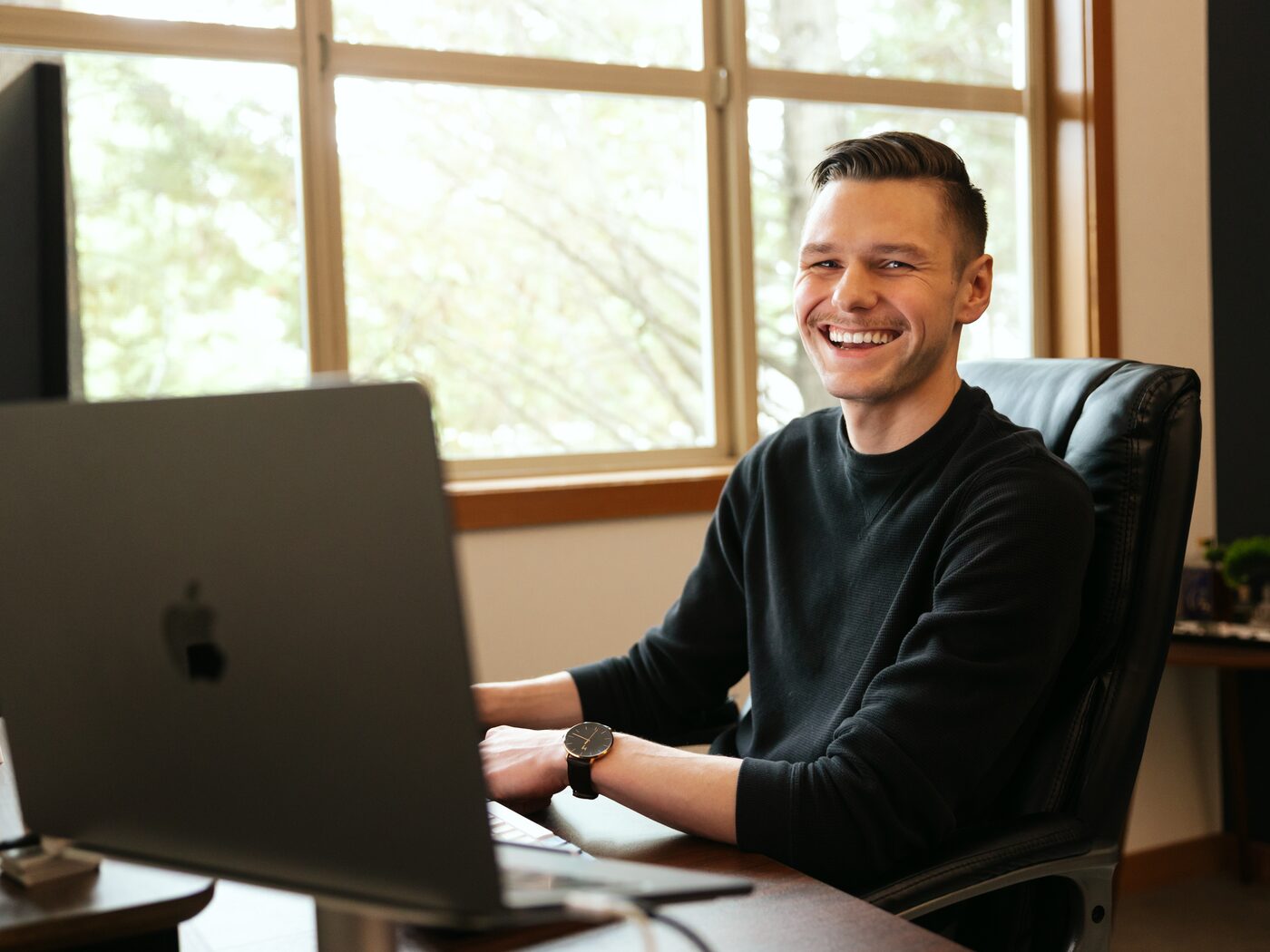 Leo Speaks smiling at his laptop by the office window