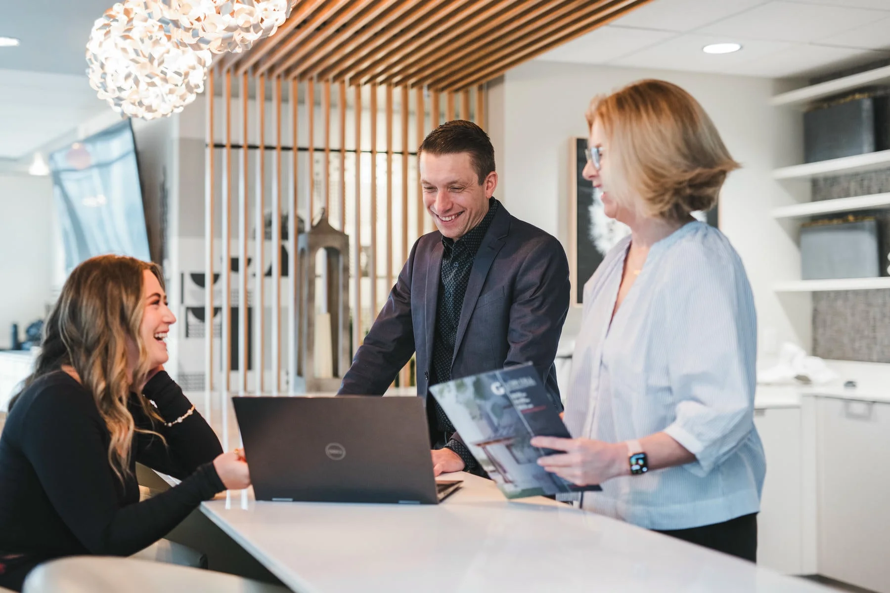 Three people in business attire gathered around a table in a modern office kitchen