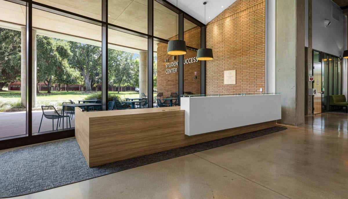 Modern student center lobby with wood and white reception desk, large windows, and pendant lights