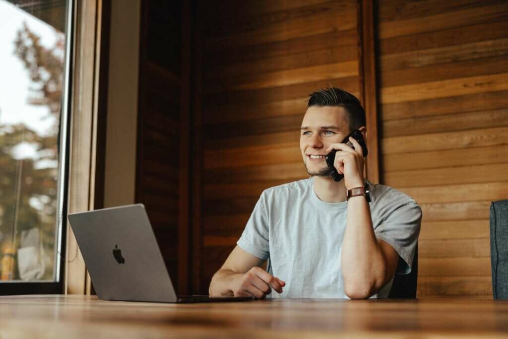 Business owner on a phone call, smiling while reviewing marketing options on a laptop