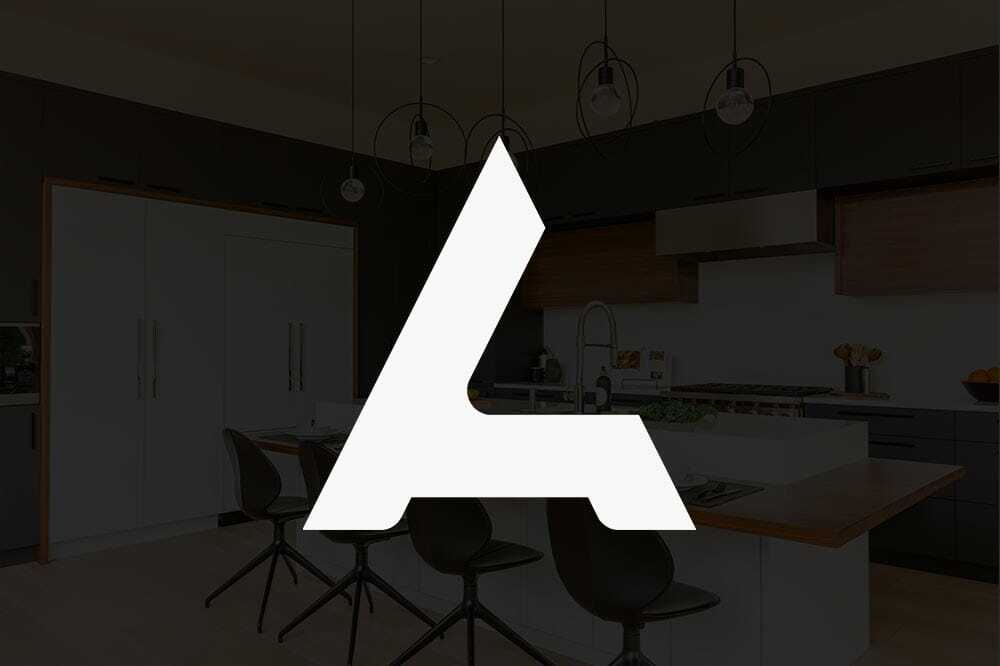 Large white abstract A logo overlay on a dimly lit modern kitchen. The kitchen has a center island with chairs, hanging lights, and dark cabinetry.