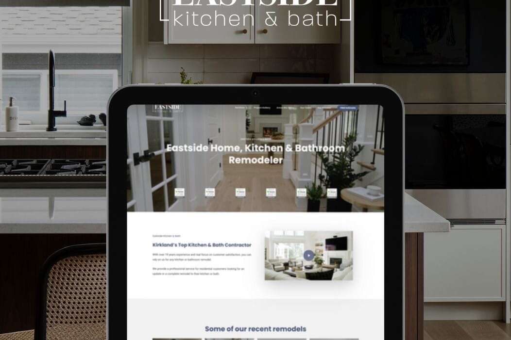 A tablet displaying a website for Eastside Kitchen & Bath, featuring images of renovated kitchens and bathrooms. The background shows a modern kitchen with sleek appliances and cabinetry. The brands logo is prominently displayed at the top.