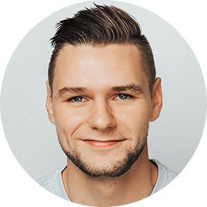A young man with short brown hair and a neatly trimmed beard smiles softly at the camera. He is wearing a gray shirt against a plain light gray background.