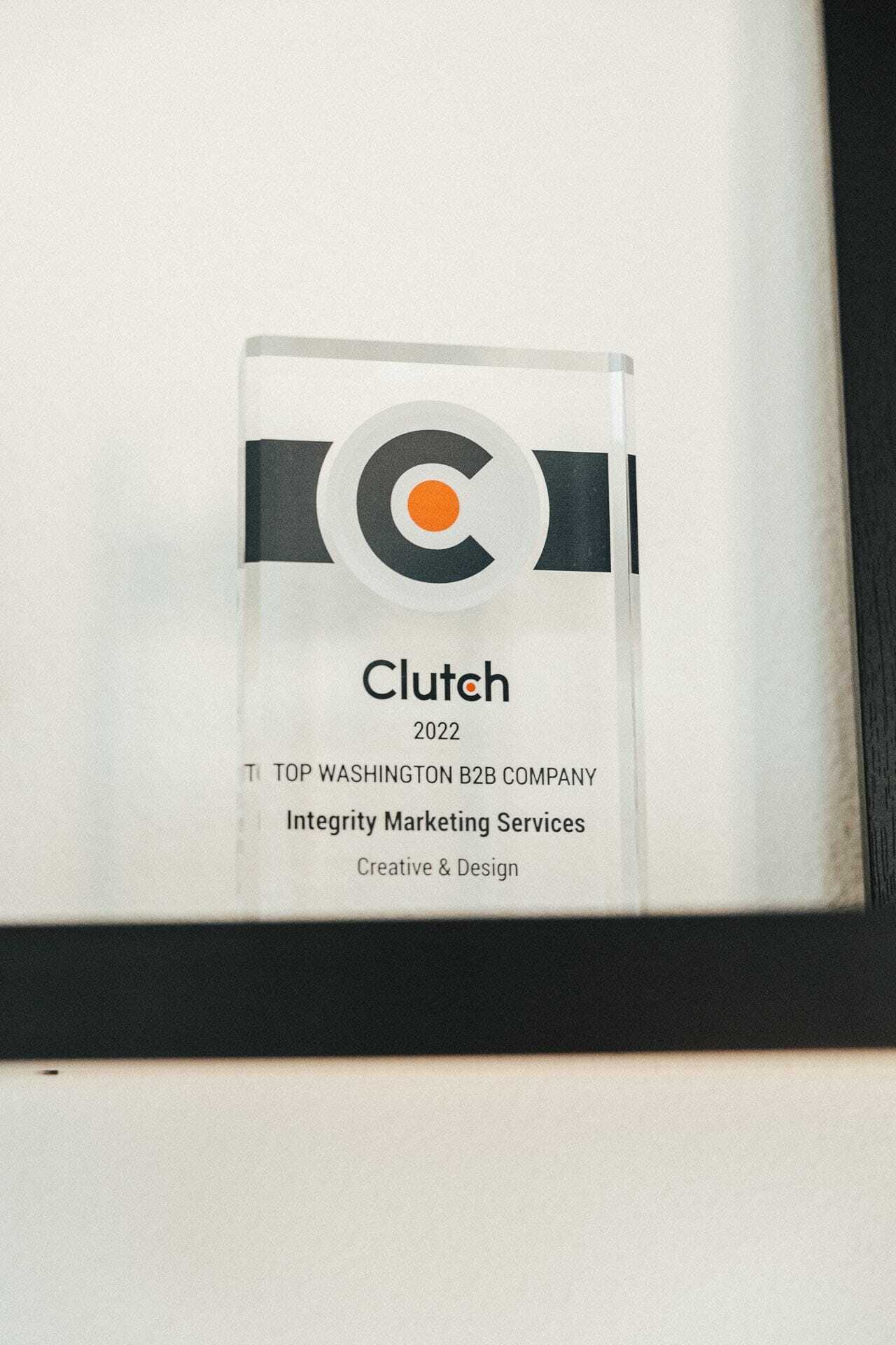 A glass award with the Clutch logo on it, recognizing a company as a 2022 Top Washington B2B Company in Integrity Marketing Services for Creative & Design. The award stands on a black shelf.