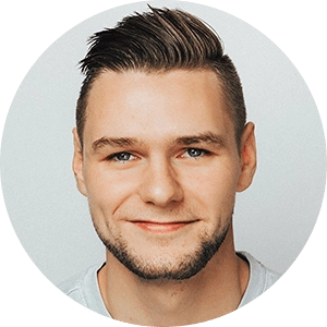 A young man with short brown hair and a neatly trimmed beard smiles softly at the camera. He is wearing a gray shirt against a plain light gray background.