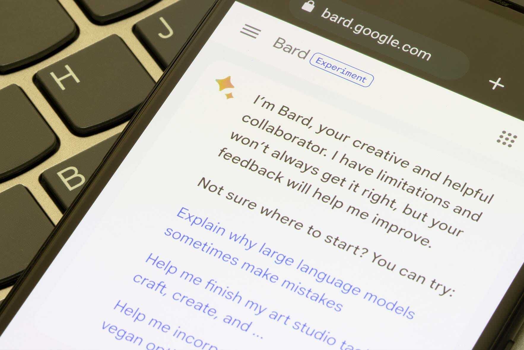 A smartphone displays a webpage with text stating, Im Bard, your creative and helpful collaborator. I have limitations and wont always get it right, but your feedback will help me improve. A keyboard is partially visible in the background.