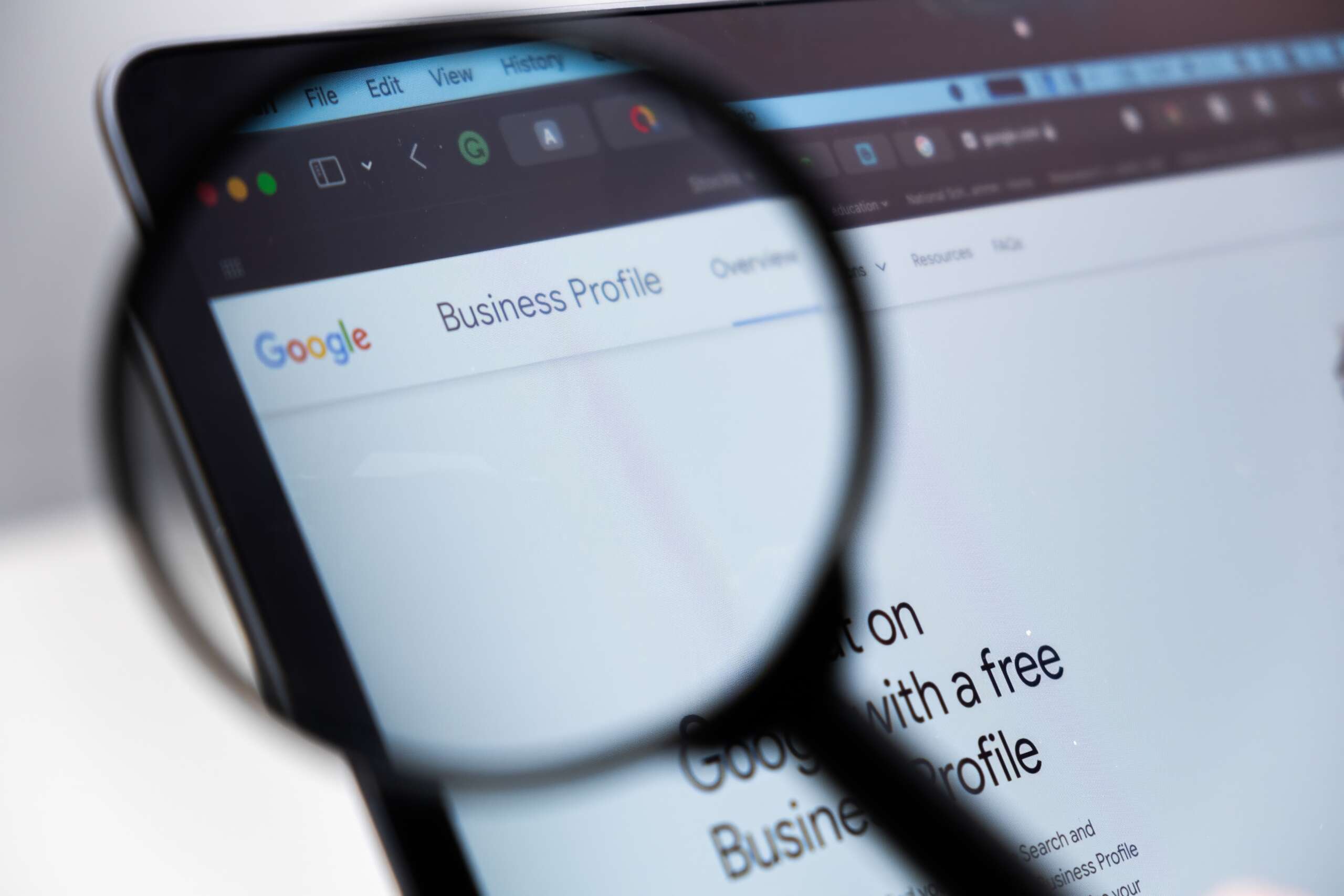 A magnifying glass is focusing on a computer screen displaying the Google Business Profile page. The URL bar and part of the content, Business Profile, are visible, suggesting the webpage is being examined closely.