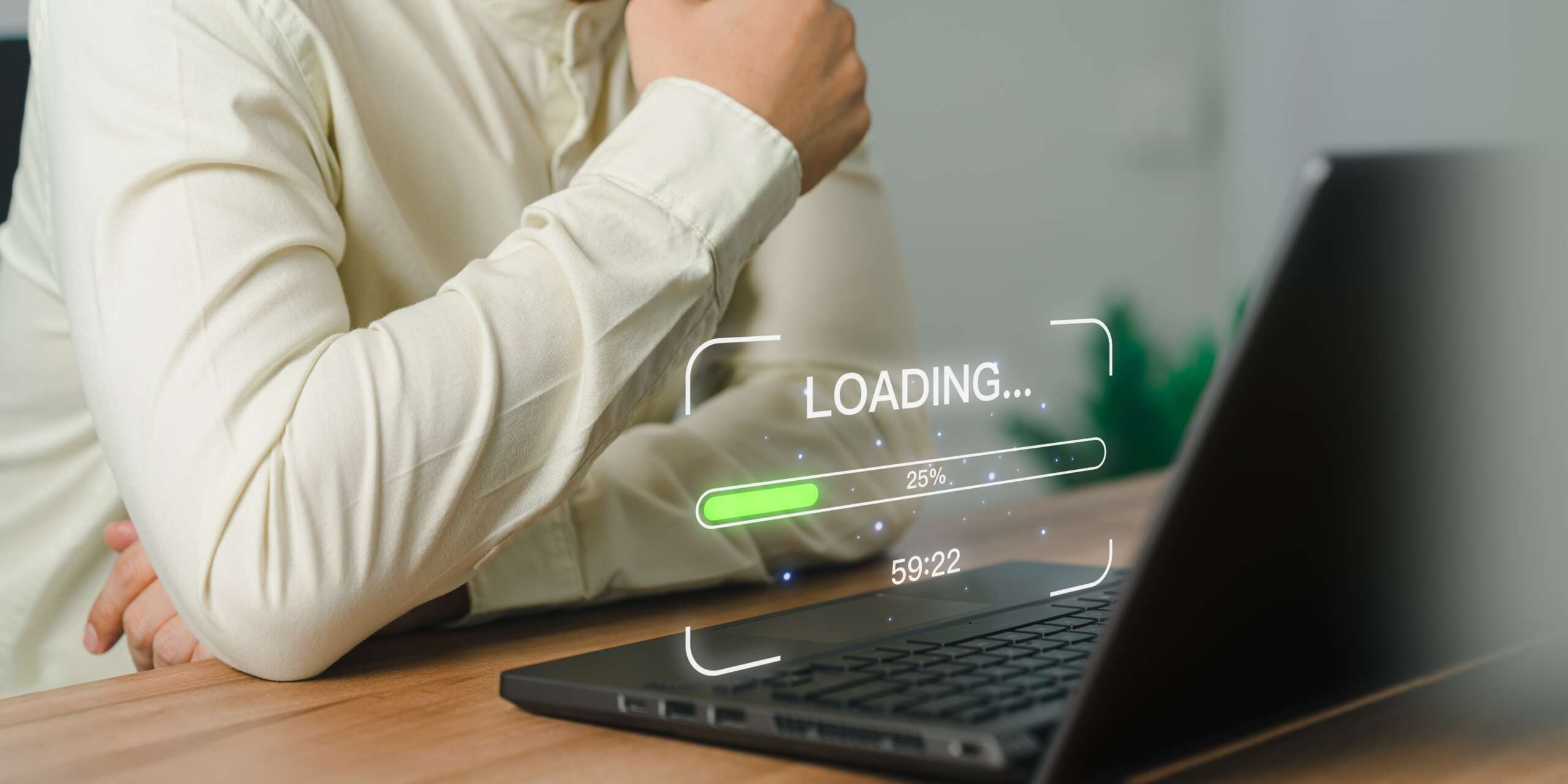 Person in a white shirt sits at a wooden table, looking at a laptop with a loading screen displaying 25% progress and a time of 59:22.