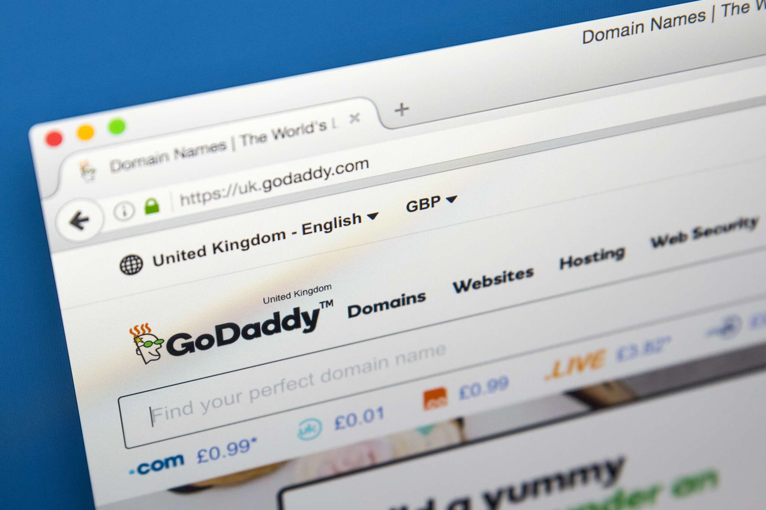 Close-up of a web browser displaying the GoDaddy UK website. The page features options for domain registration, websites, hosting, and web security. The URL is visible, showing https://uk.godaddy.com with currency set to GBP.