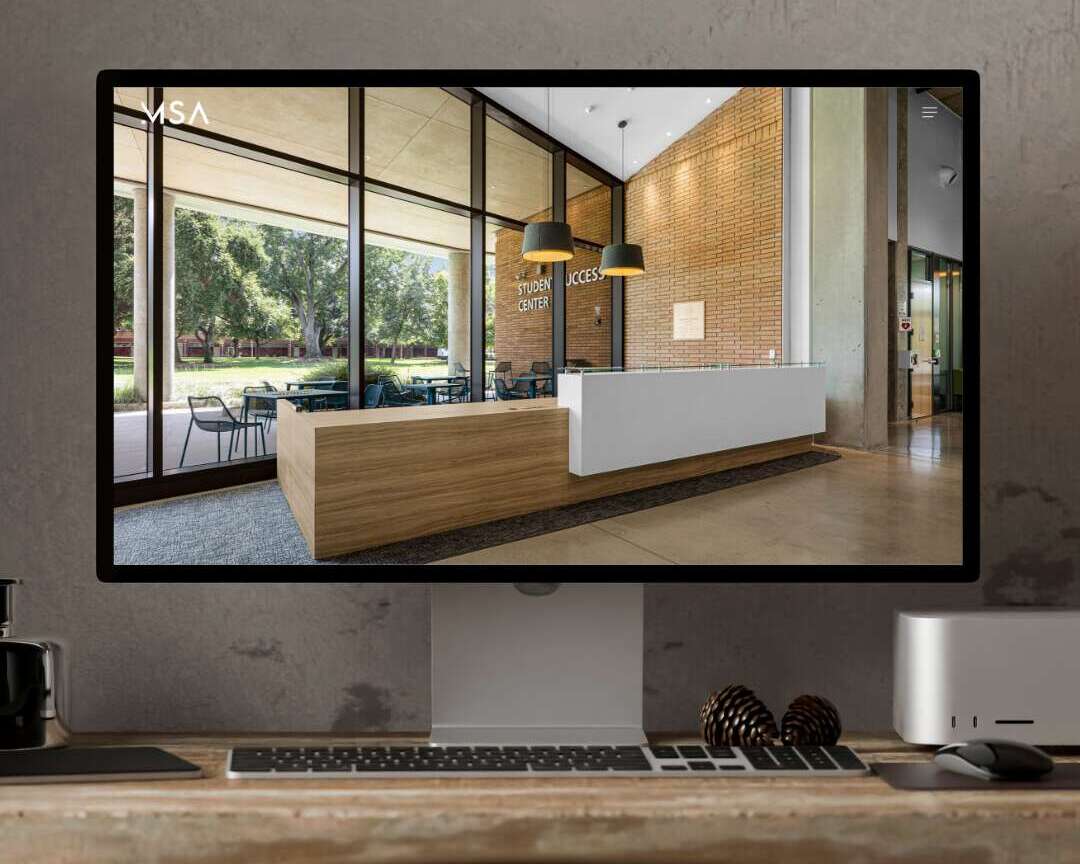 A computer monitor on a desk displays an image of a modern, well-lit reception area with large windows, wooden furniture, and a sign reading Student Center Access.