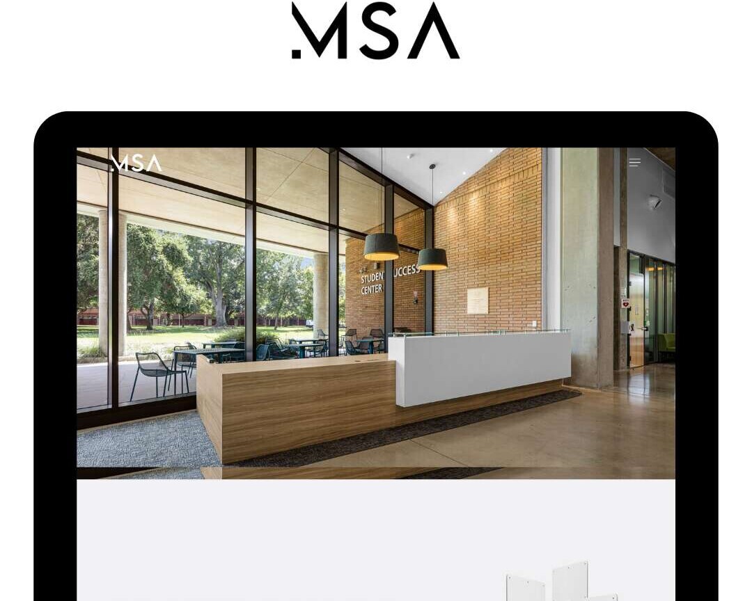 A modern office reception area with a sleek wooden desk, white panel, and large windows letting in natural light. The image is displayed on a device screen with the MSA logo above it.