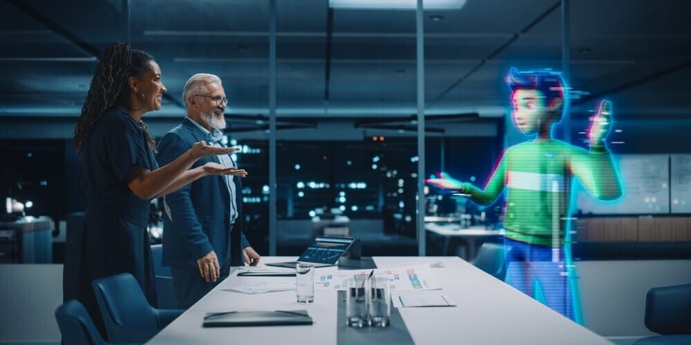Two people in a modern office interact with a holographic avatar. The room is dimly lit, with large windows showing a cityscape at night. A long table is in the foreground with various documents and a conference phone.