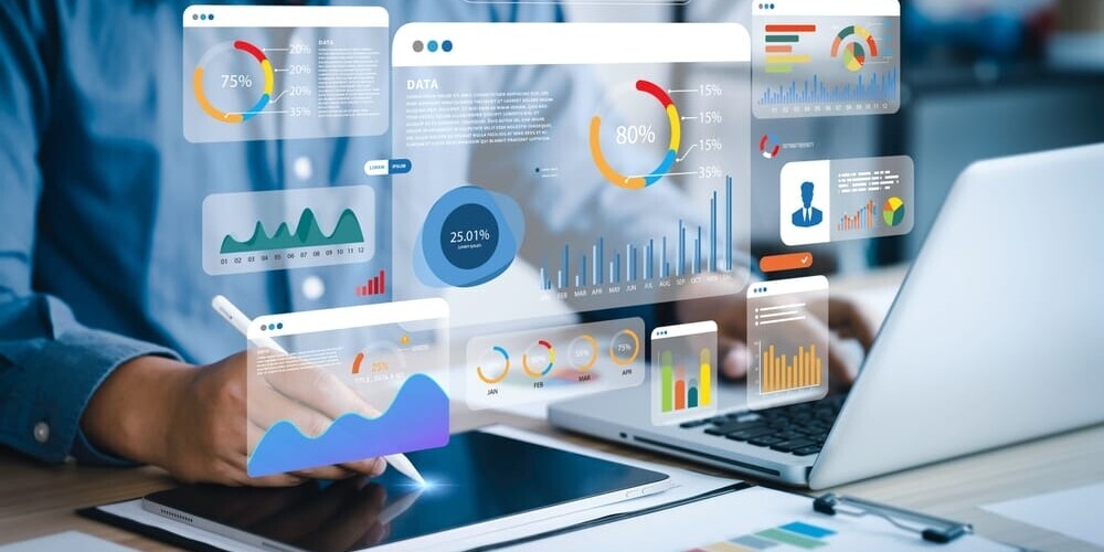 A person using a tablet and laptop displays various colorful graphs and charts. The floating analytics include pie charts, bar charts, and line graphs, illustrating data analysis and statistics in a digital workspace.