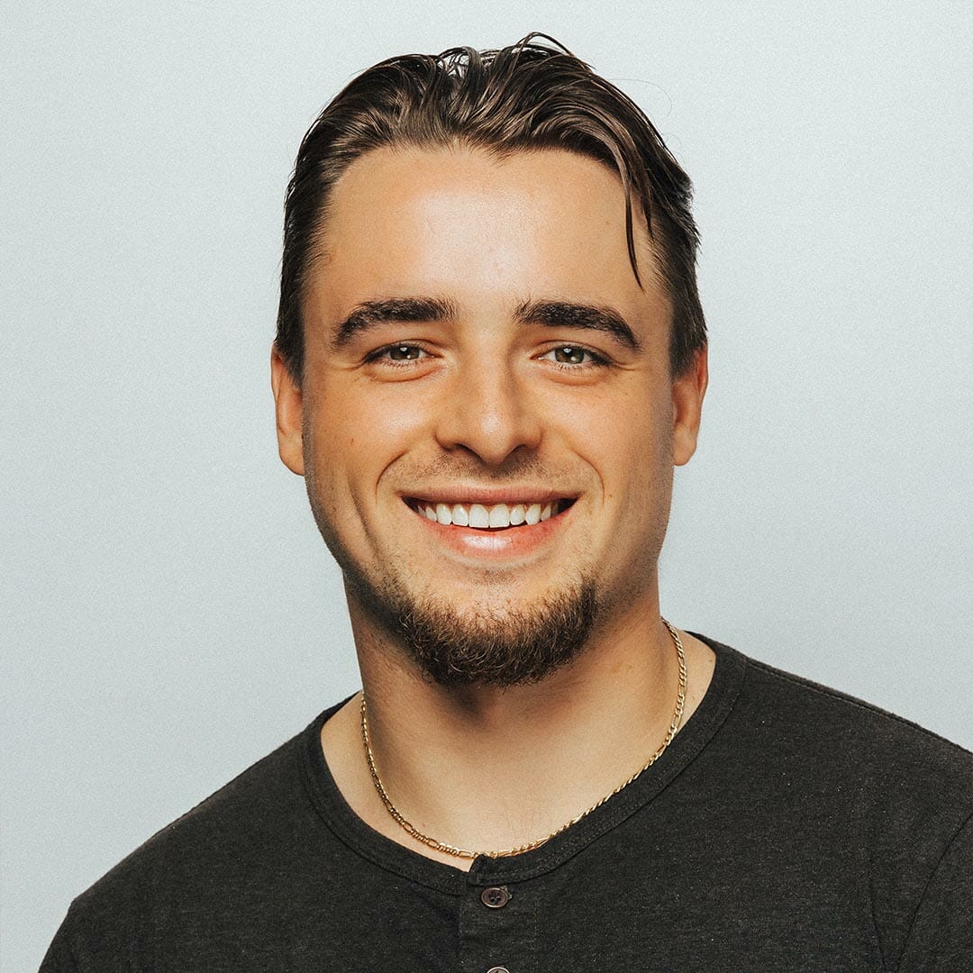 Smiling person with short hair and a goatee, wearing a dark shirt, against a plain background.