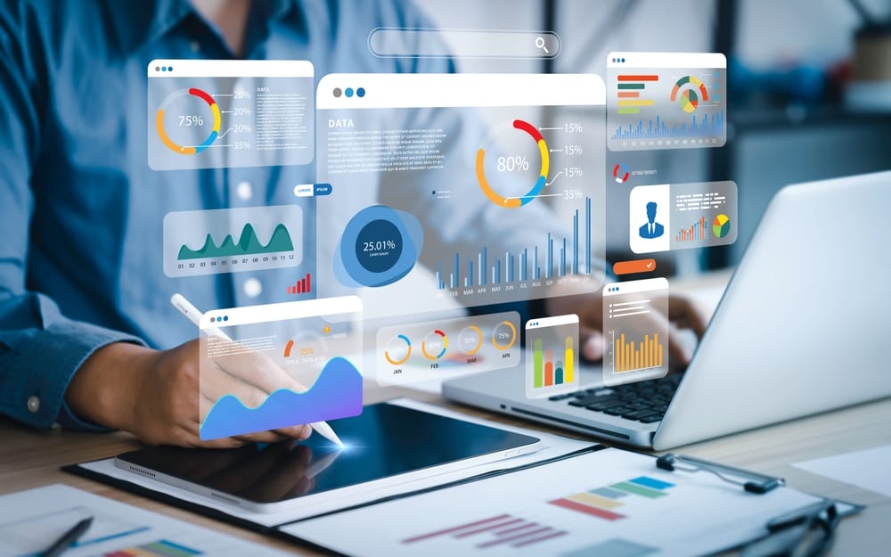 A person using a tablet and laptop displays various colorful graphs and charts. The floating analytics include pie charts, bar charts, and line graphs, illustrating data analysis and statistics in a digital workspace.