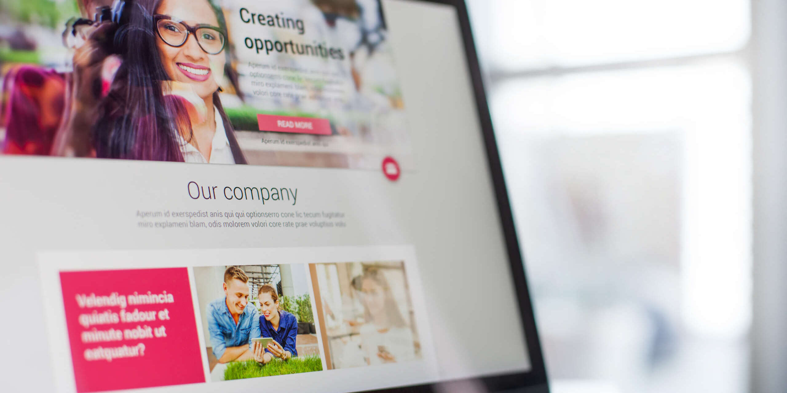 Laptop screen displaying a website with sections titled Creating opportunities and Our company. It includes images of a smiling woman with glasses and a man and child playing with a toy rocket. A red button labeled Read More is visible.