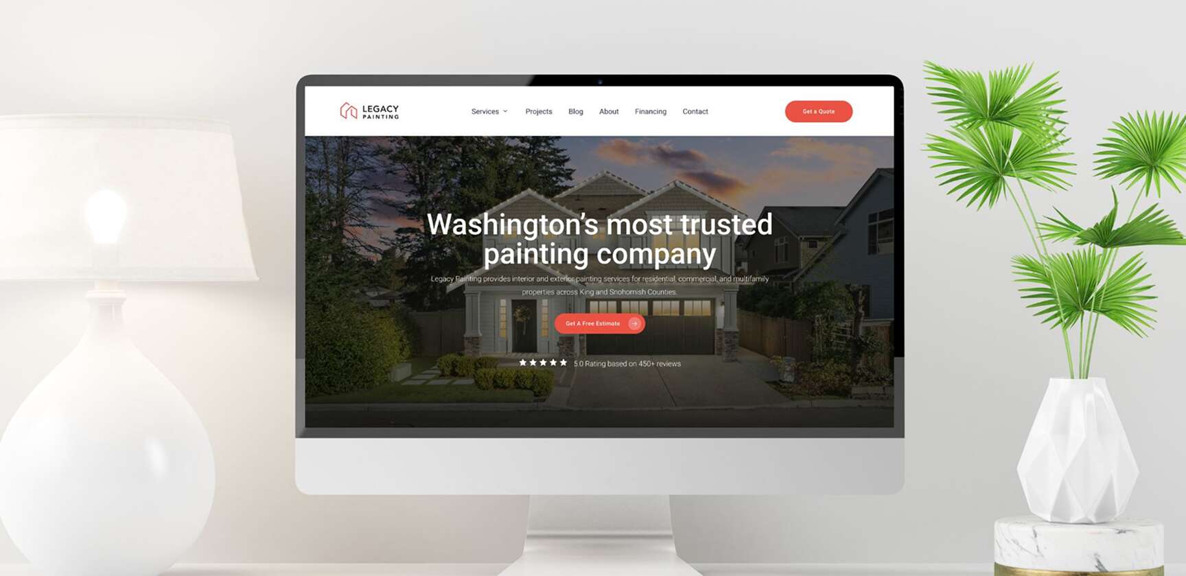 A computer monitor on a white desk displays a website for Legacy Painting, featuring a house, the text Washingtons most trusted painting company, and a red Get a free estimate button. A green plant is to the right of the monitor.